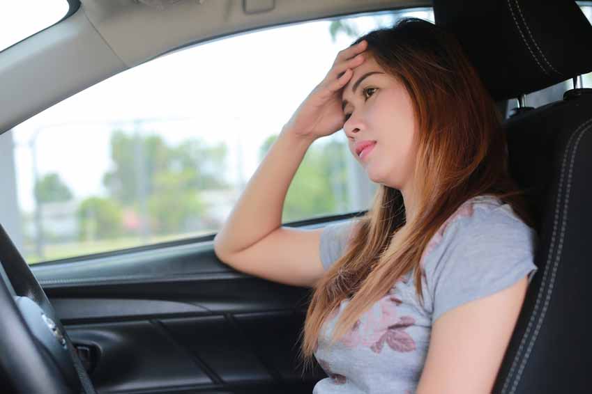 Young woman seems to be struggling with driving nerves as she sits in the driving seat of a car.