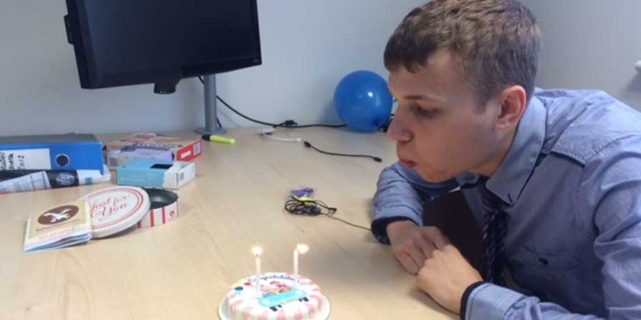a photo of a male blowing out the candles on a small cake